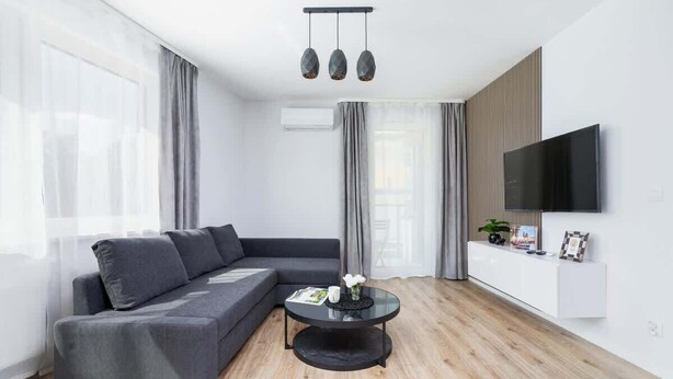 A modern living room with a grey sectional sofa, a round coffee table, and a flat-screen TV mounted on the wall. - Modern Apartment | Balcony, Close to Center (Kraków)