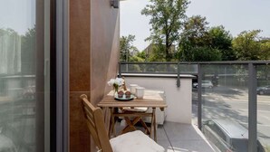 A balcony with a table set for two, a chair, and a view of the street and trees. - Modern Apartment | Balcony, Close to Center (Kraków)