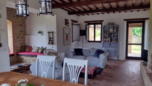 A cozy living room with a wooden ceiling, a white sofa, a dining table with a green tray, and a bookshelf.