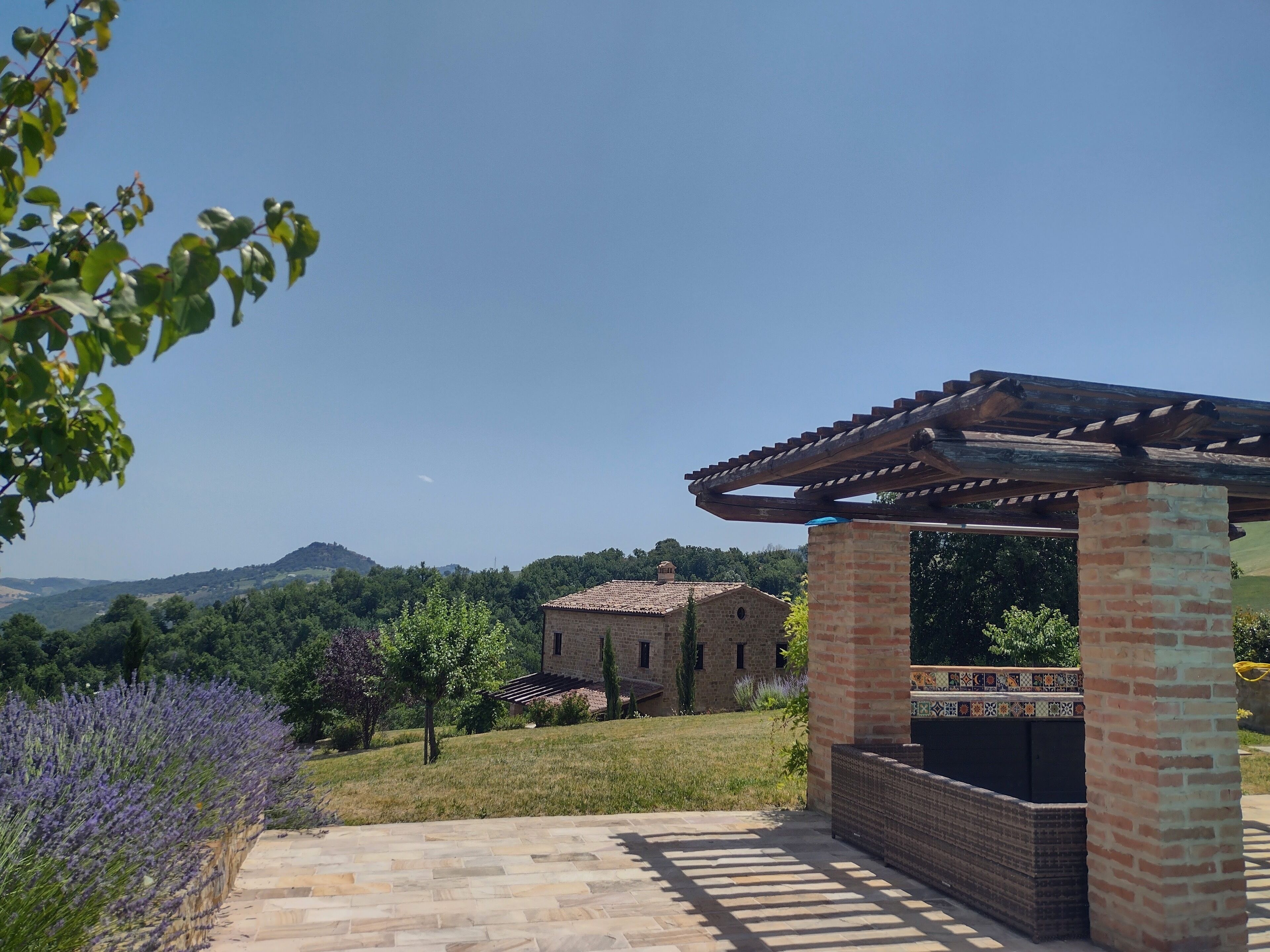 A patio area with a pergola, a brick column, and a view of a distant building.
