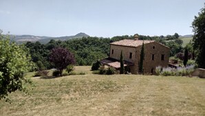 A rustic stone building with a tiled roof, surrounded by a grassy field and dense trees.