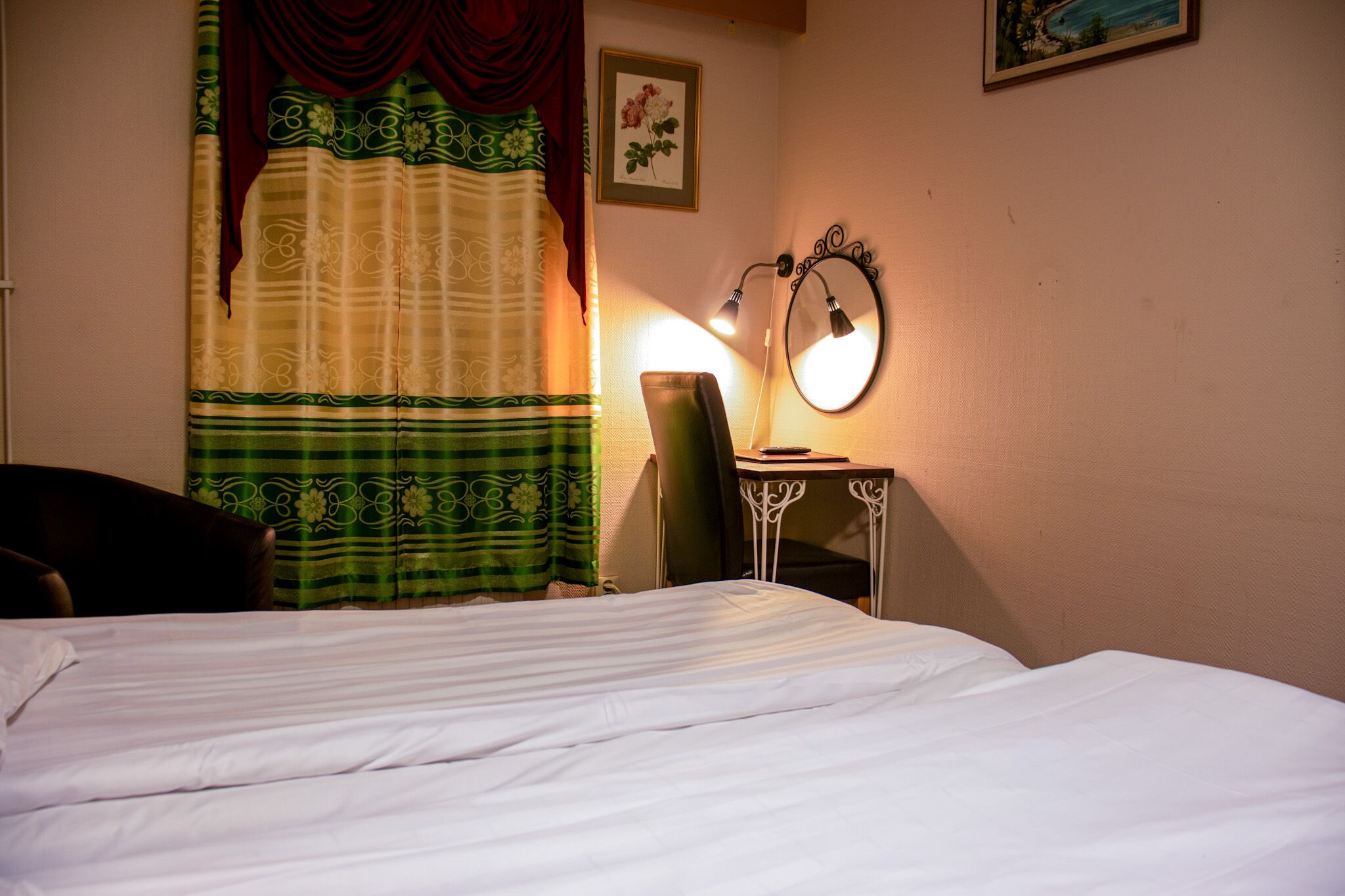 Habitació d'hotel amb un llit, un escriptori amb una cadira, una làmpada i un mirall.