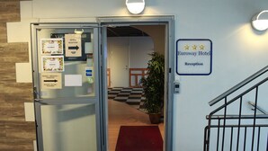 A hotel reception area with a glass door, a red mat, and a sign indicating the reception.
