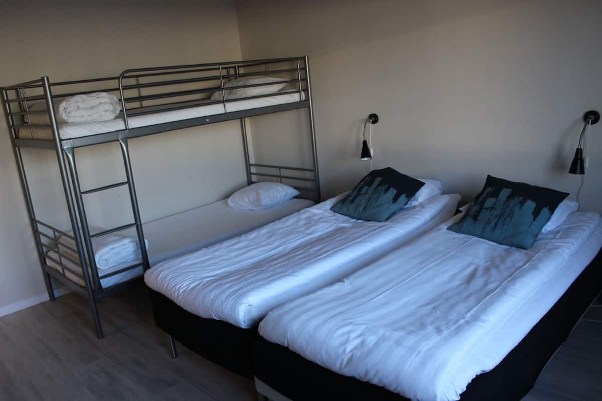 A bunk bed with white bedding and a lower bed with a black headboard. There are two wall-mounted lamps on either side of the lower bed.