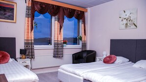 A hotel room with two beds, a desk, a chair, and a window with curtains.