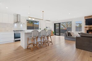 A modern kitchen with white cabinets, a central island with bar stools, a large window, and a fireplace.