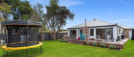 A backyard with a trampoline, a wooden deck, and a house with a covered patio.