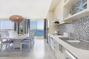 A modern kitchen with a large island, a view of the sea, and a dining area with a view. - Blouberg Heights 1601 by HostAgents (Cape Town)