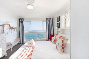 A bedroom with a large bed, a desk, and a view of the ocean.