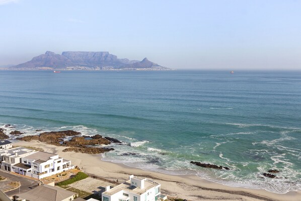 A coastal view with a beach, rocky shoreline, and a distant mountain.