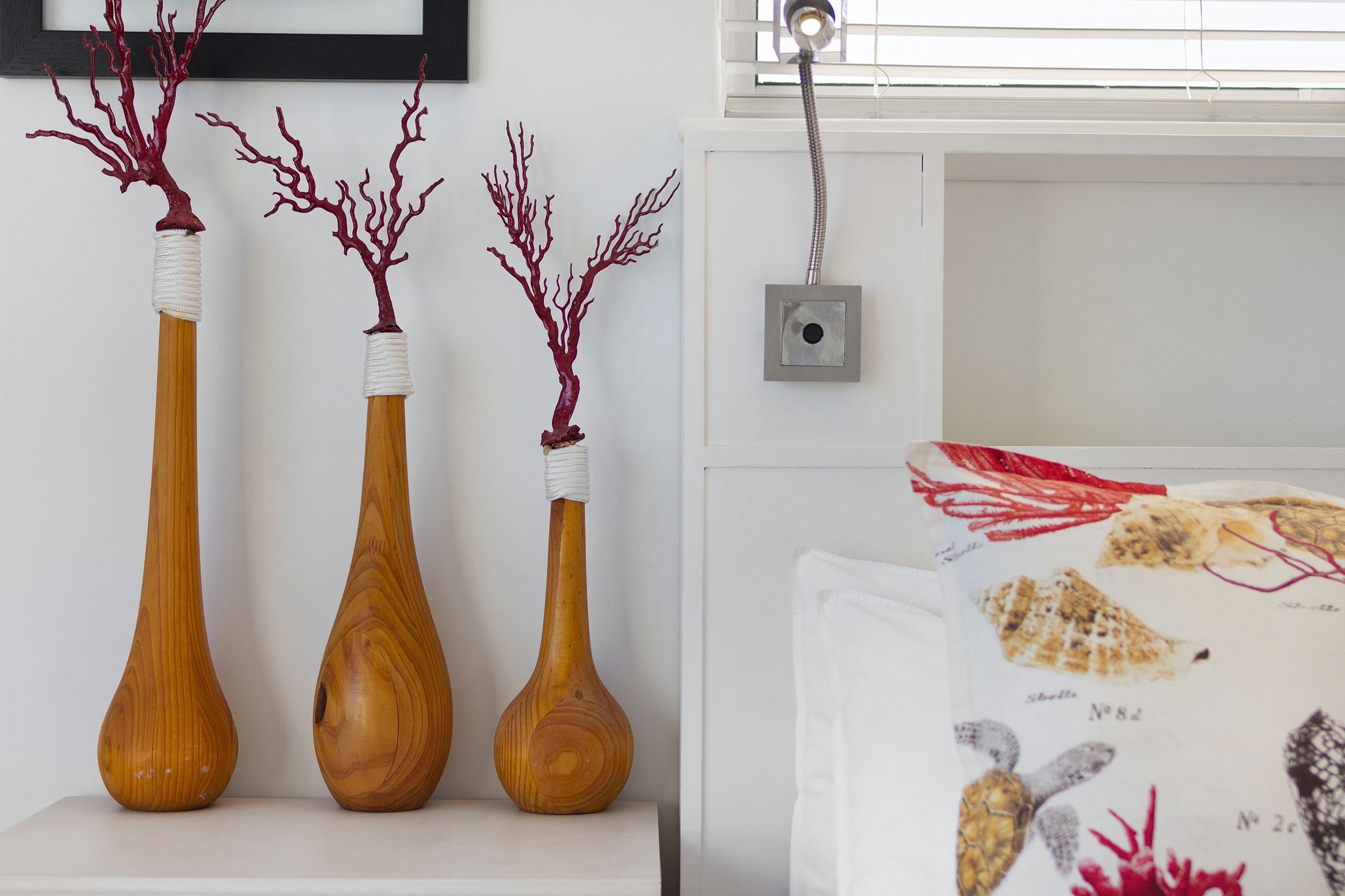 Three wooden vases with red coral decorations on a white shelf.