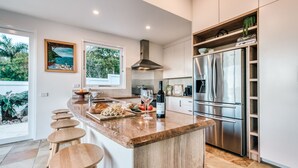 A modern kitchen with a central island, stainless steel appliances, and a view of greenery outside. - Villa Sunshine - 200m to beach, ocean views, 5mins to Hastings St (Sunshine Beach)