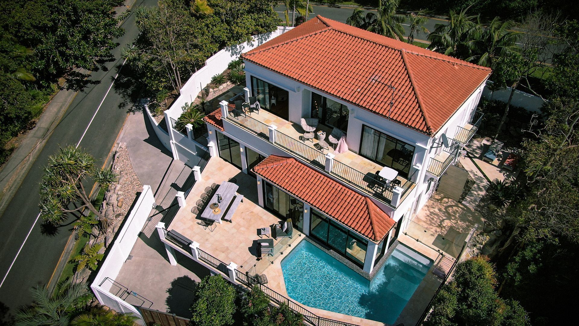 A two-story house with a swimming pool, a balcony, and a view of the surrounding greenery.