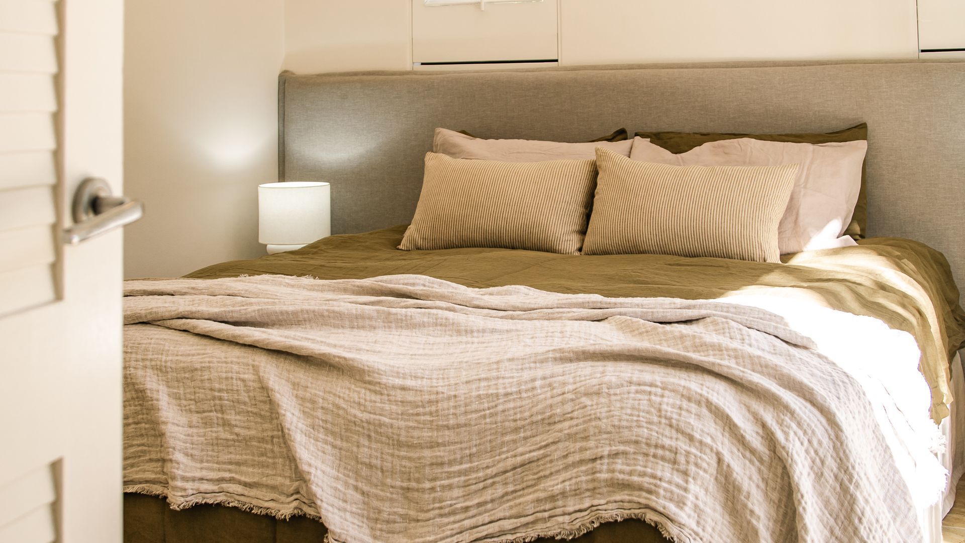A neatly made bed with a beige and brown striped blanket, a matching pillow, and a bedside lamp.