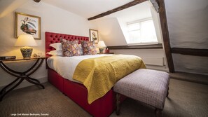 Relax in this spacious master bedroom with a comfortable red upholstered bed, featuring a nightstand, lamp, and framed botanical prints.