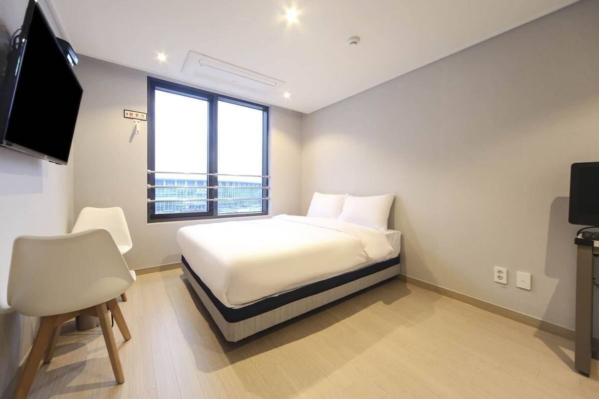 Habitación de hotel con cama, una silla, televisor, ventana con vista y una lámpara en el techo.