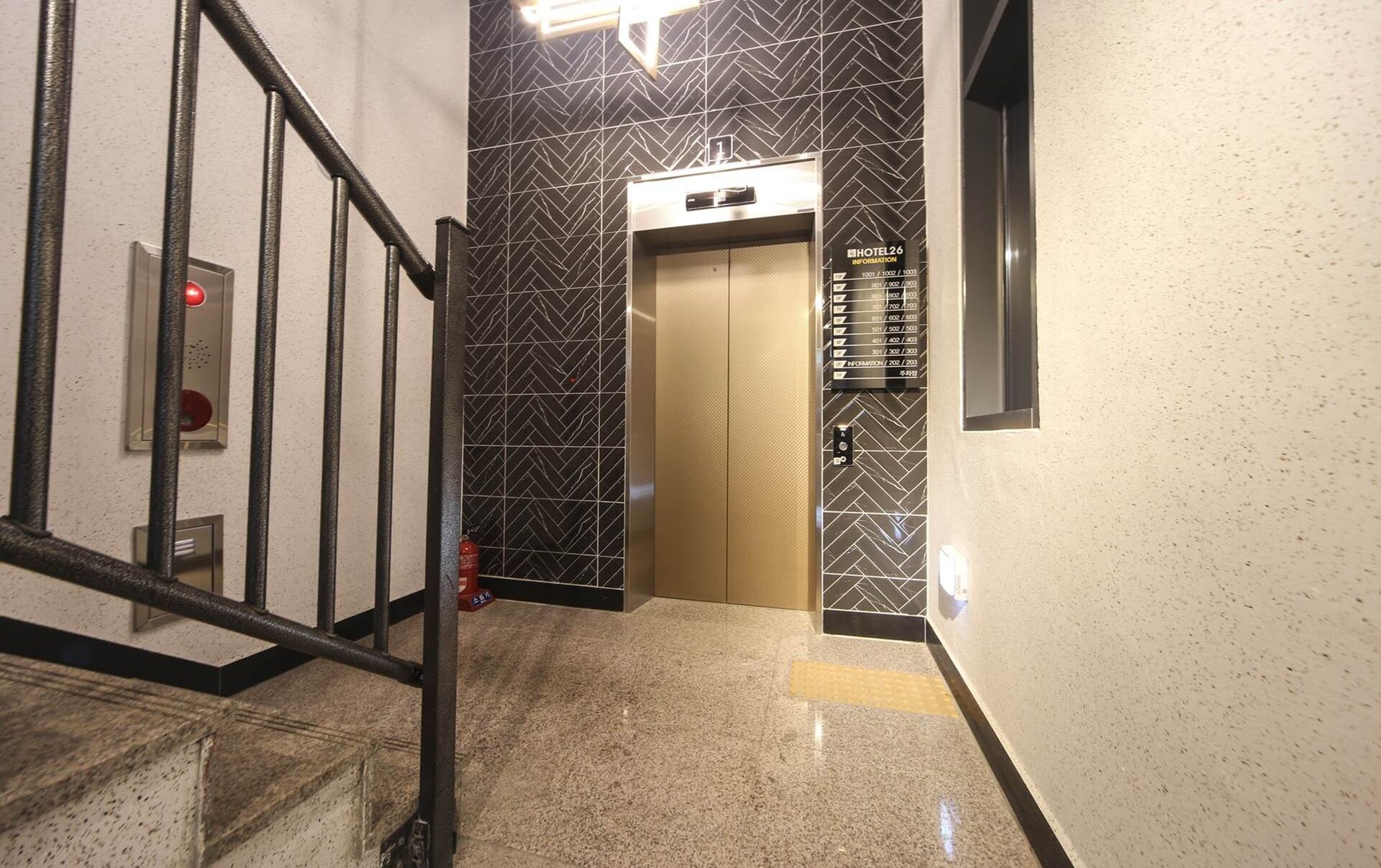 Un ascensor en un pasillo con pared de diseño blanco y negro, una alarma de incendios y un extintor.