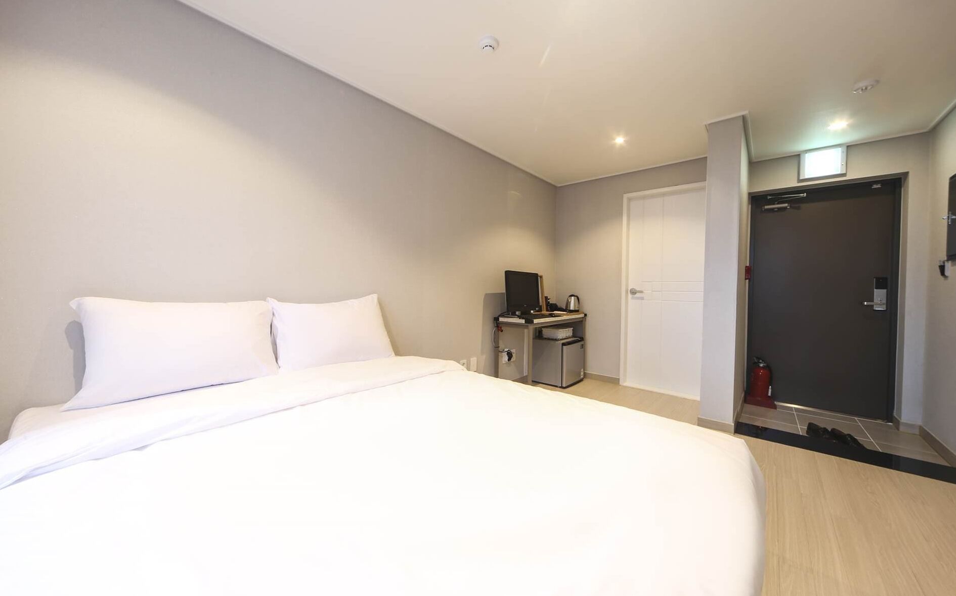 Een moderne hotelkamer met een groot bed, een bureau met een computer, een kleine koelkast en een deur naar een badkamer.
