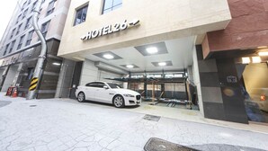 Entrada de hotel con un coche blanco estacionado frente a él.