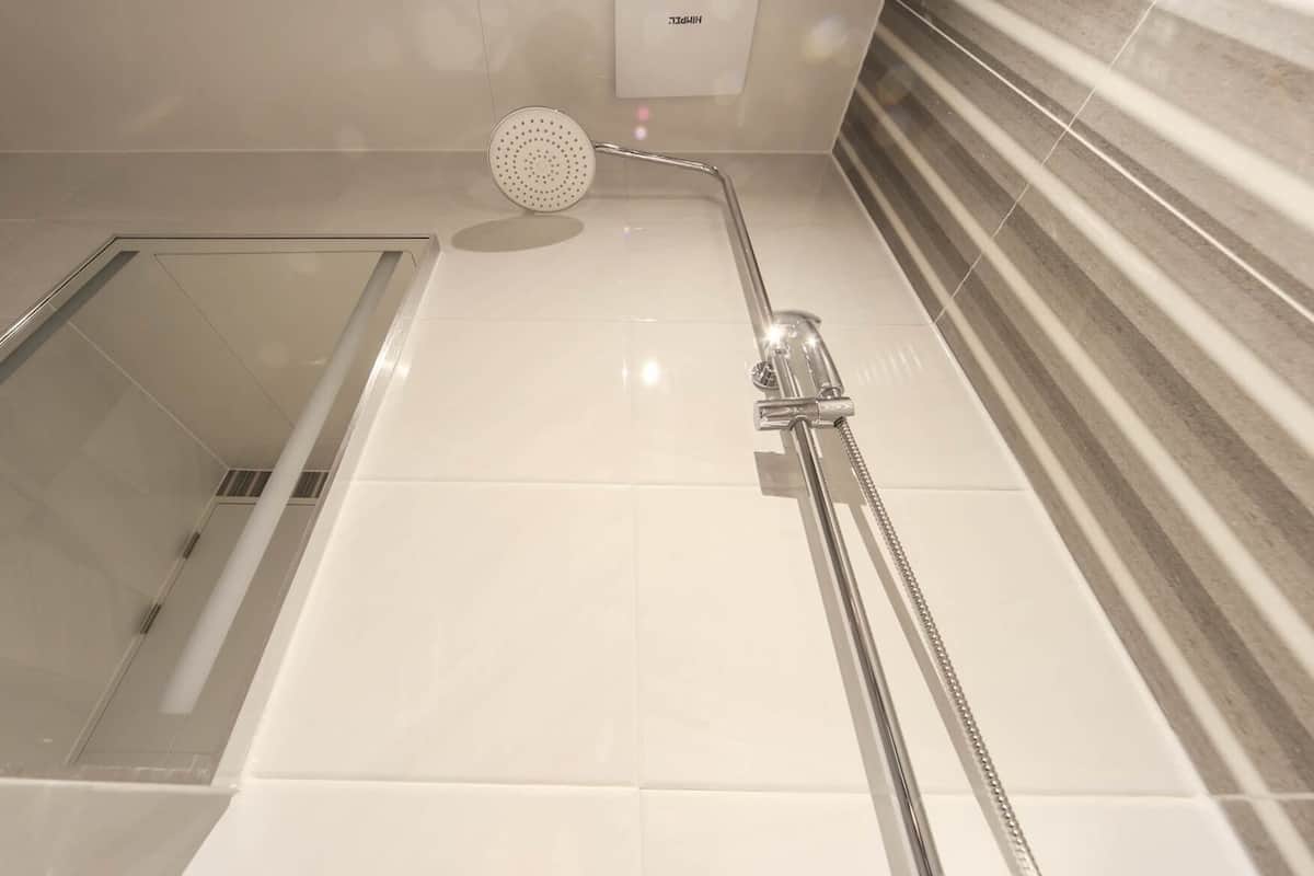 Un área de ducha con cabezal de ducha de mano, cabina de ducha con mampara de vidrio y pared revestida de azulejos.