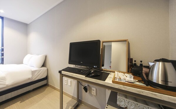 A hotel room with a bed, a desk with a computer, a mirror, and a kettle. - Hotel 26 (Busan)