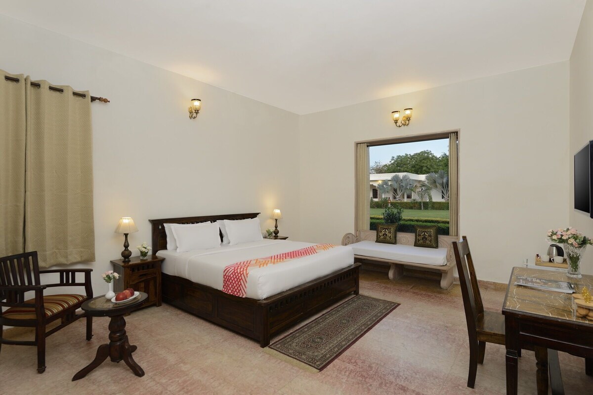 A hotel room with a large bed, bedside tables, a chair, a desk, a window with a view, and wall-mounted lights.