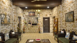 A lobby with stone walls, a reception desk, seating area, and a ceiling fan. - Ginger Ranthambore,Sawai Madhopur (Sawai Madhopur)