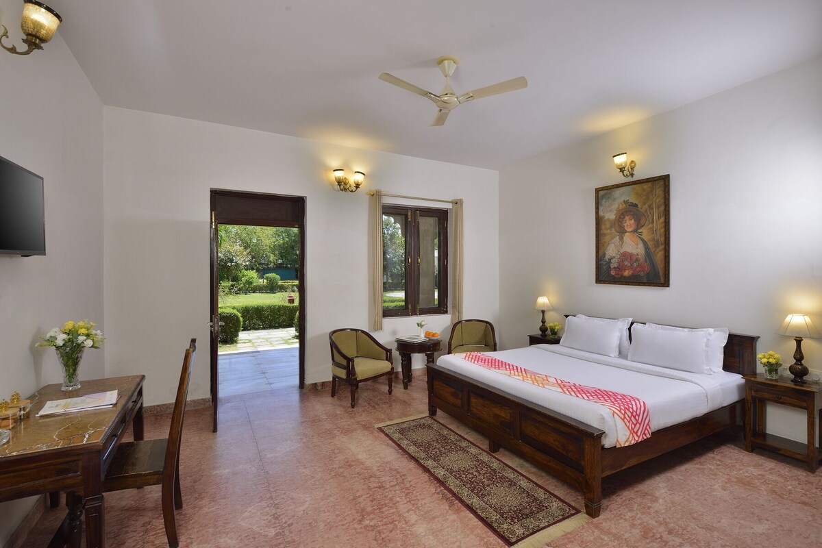 A bedroom with a bed, bedside tables, a desk, chairs, a ceiling fan, and a painting on the wall.
