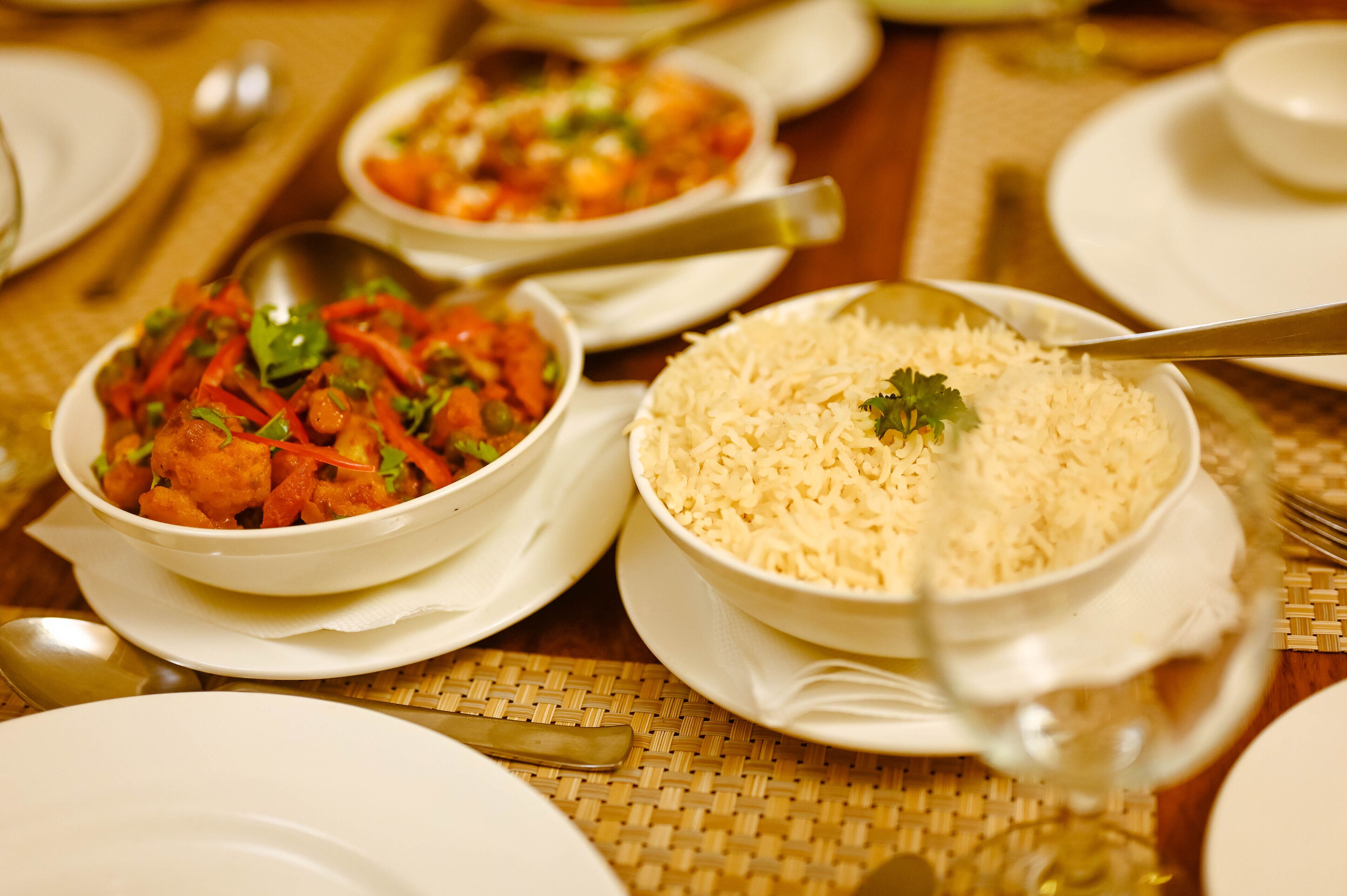 A table set with white plates, bowls of rice, and a bowl of vegetable curry.