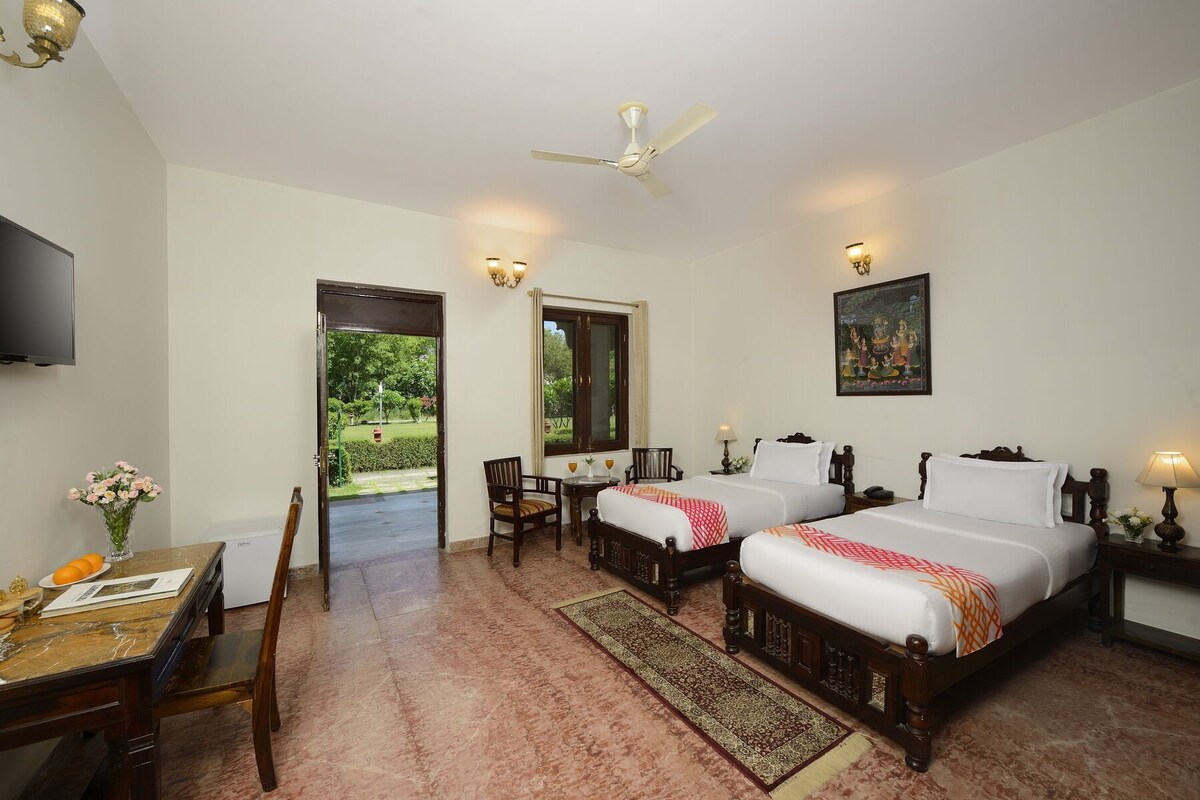 A hotel room with two beds, a desk, a chair, a TV, and a ceiling fan.