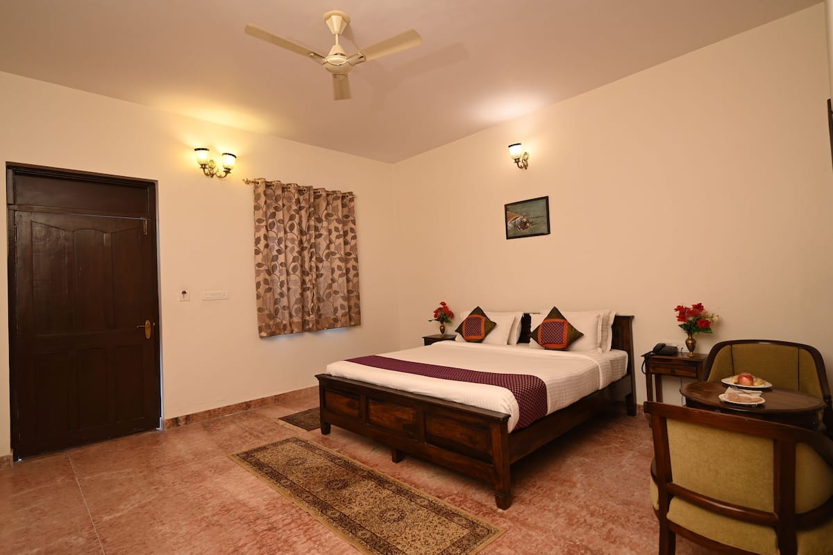 A bedroom with a bed, a nightstand, a chair, a door, a ceiling fan, and a wall-mounted light fixture.