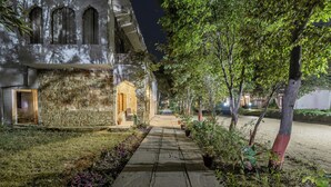 A stone pathway leading to a building with arched windows and a door, surrounded by greenery and potted plants. - Ginger Ranthambore,Sawai Madhopur (Sawai Madhopur)