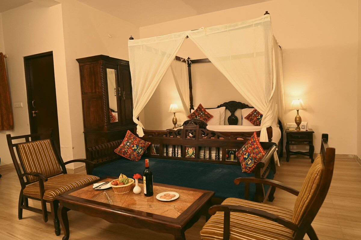 A traditional room with a four-poster bed, a dining table with chairs, a wooden cabinet, and two bedside tables with lamps.