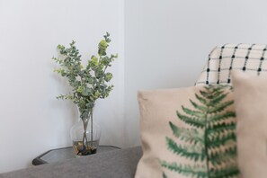 A clear glass vase with green foliage on a glass table against a white wall.