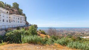 A hillside hotel with multiple balconies, a stone retaining wall, and a view of the distant landscape. - Holiday Home 'Casa La Puente' with A/C (Mijas)