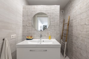 A bathroom with a white sink, a round mirror, and patterned tiles.