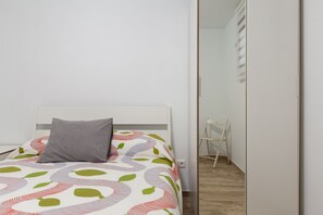 A bedroom with a bed, a grey pillow, a colorful blanket, a wooden floor, and a white wardrobe.