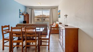 A dining area with a table and chairs, a sofa, a cabinet, and a view through a large window. - Apartment "Golden Dream" with Sea View, Balcony & Wi-Fi (Porto Santo)