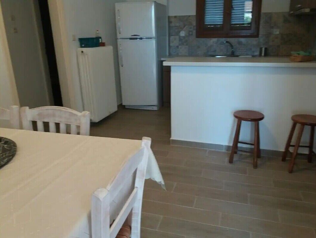 Een keuken met een witte koelkast, een klein eiland met krukken en een betegelde vloer.