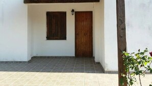 A covered entrance with a wooden door and window, tiled floor, and a small plant. - Apartment 'Μaria's House 1' with Private Terrace, Shared Garden and Air Conditioning (Evias)