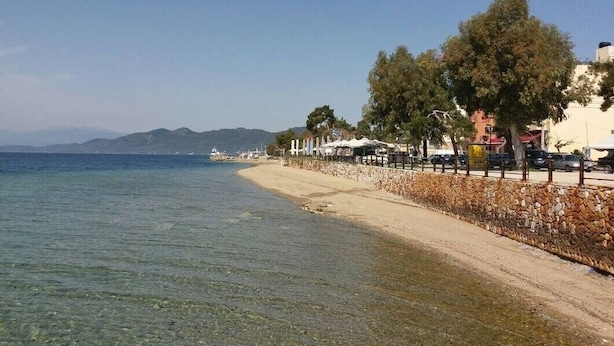 A beach with clear water, a stone wall, and buildings in the background. - Apartment 'Μaria's House 1' with Private Terrace, Shared Garden and Air Conditioning (Evias)