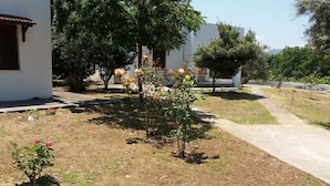 A residential area with a white building, a paved path, and a small garden with flowering plants. - Apartment 'Μaria's House 1' with Private Terrace, Shared Garden and Air Conditioning (Evias)