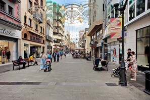 A pedestrian street lined with shops and cafes, benches, and people walking.