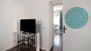 Ein Zimmer mit einem auf einem Schrank stehenden Fernseher, einer Tür mit einem dekorativen Rundmuster und einem Blick in einen Essbereich im Hintergrund.