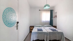 Ein kleiner, sauberer Raum mit zwei Betten, einer Hängelampe und einem dekorativen Wandmuster.