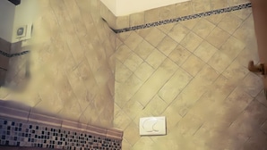 A bathroom with a tiled wall, a wooden ceiling beam, and a tiled backsplash.