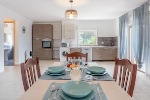 Une cuisine moderne avec des meubles en bois, une table à manger dressée avec de l’assiette, et une vue sur l’extérieur.