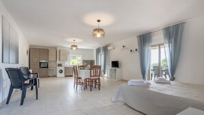 A modern hotel room with a bed, a desk, a chair, a dining table, and a kitchenette.
