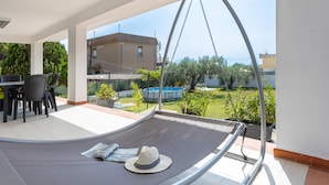 A hammock with a hat, a table with chairs, and a view of a pool and greenery.