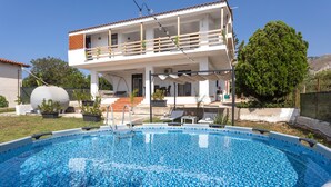 A two-story building with a swimming pool, outdoor furniture, and potted plants.